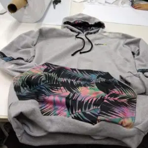 Hoodie gris con estampado tropical colorido y diseño moderno, ideal para un look casual.