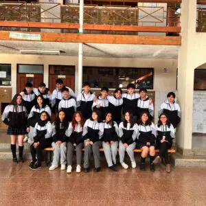 Estudiantes de 4to medio con polerones negros, sonrientes en un ambiente escolar cálido.