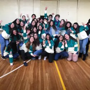 Jóvenes del 4to medio celebrando con polerones verdes y crema en un ambiente festivo.