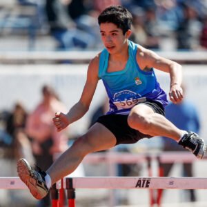 Joven atleta saltando en carrera de obstáculos, mostrando dedicación y habilidad en atletismo.