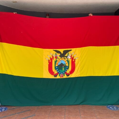 Bandera de Bolivia ondeando frente a un edificio, símbolo de orgullo y unidad nacional.