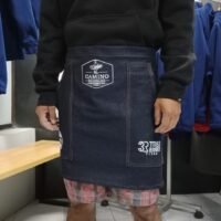 Hombre con delantal de denim y pantalones de cuadros en tienda de moda casual.