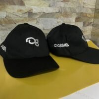 Gorras negras con bordado plateado, estilo moderno y elegante sobre fondo de piedra.