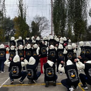 Curso 4to medio celebrando su promoción con polerones negros y capuchas en un ambiente festivo.